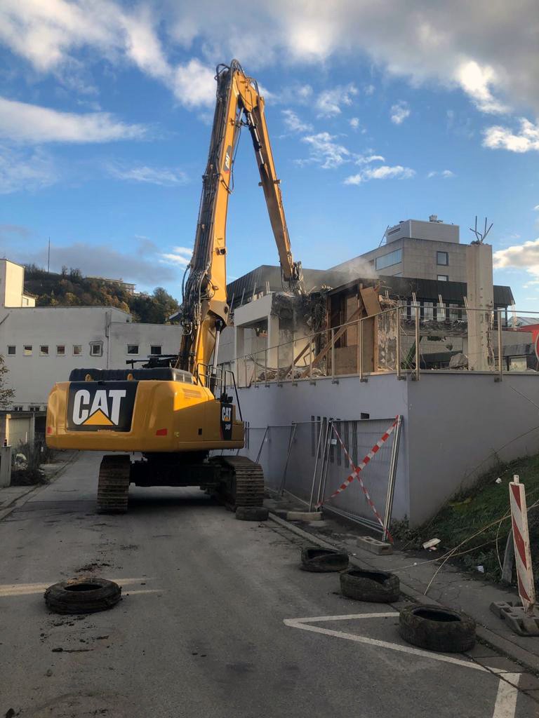 Bagger demoliert zweistöckiges Betongebäude, Trümmer und Bauschutt am Boden
