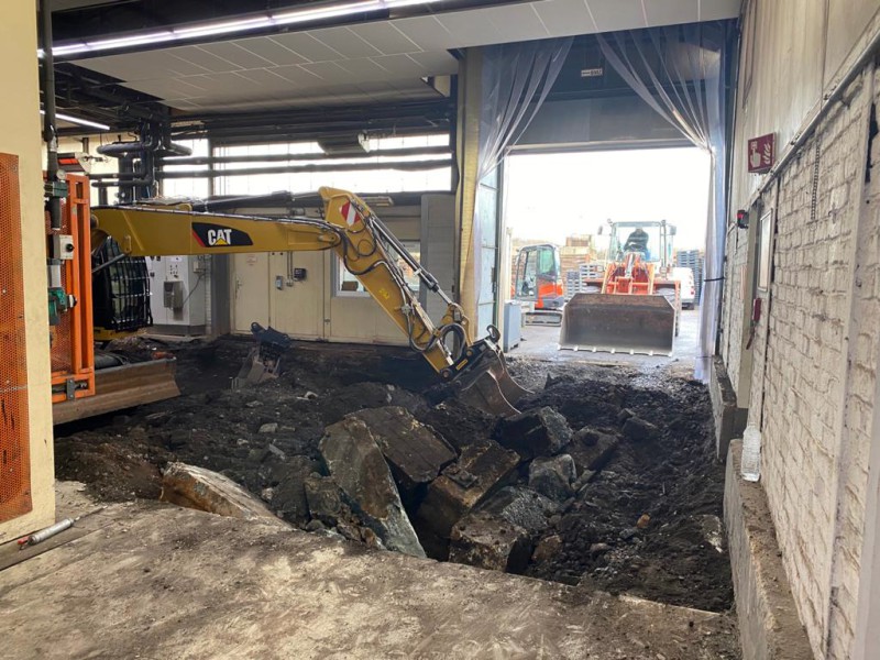 Aufgebrochene Betonbodenplatte in Industriehalle, Baggerschaufel im Bild