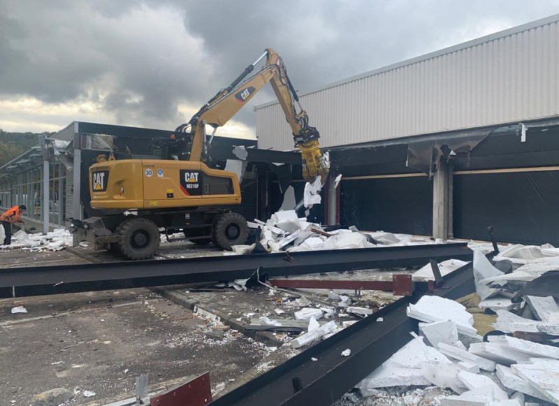 Hydraulikbagger demoliert große Industriehalle mit Glasfassade
