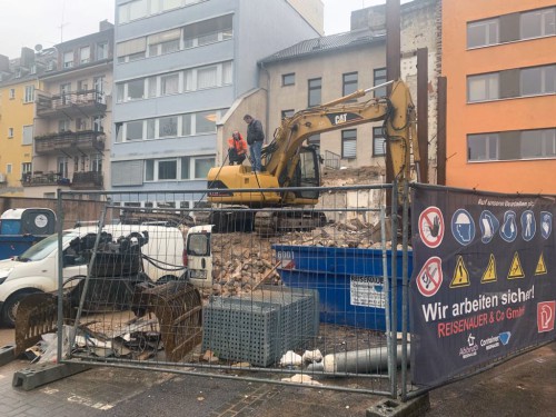 Bagger arbeitet an teilweise abgerissenem Wohngebäude mit Ziegeldach