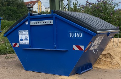 Blauer Absetzcontainer steht auf einer Baustelle neben Baufahrzeugen